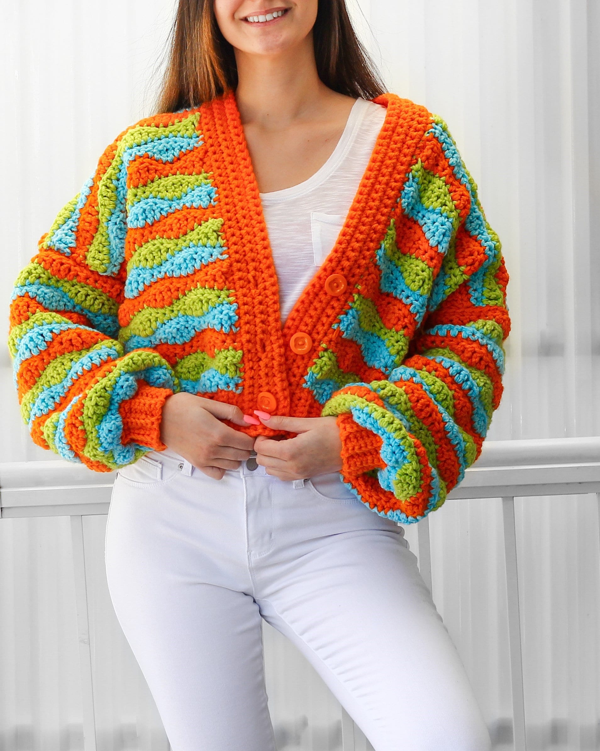May include: A cropped cardigan with a colorful striped pattern in orange, green, and blue. The cardigan has a V-neck and button closure.