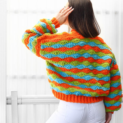 May include: A colorful crocheted sweater with orange, green, and blue stripes. The sweater has a loose fit and a slightly cropped length.
