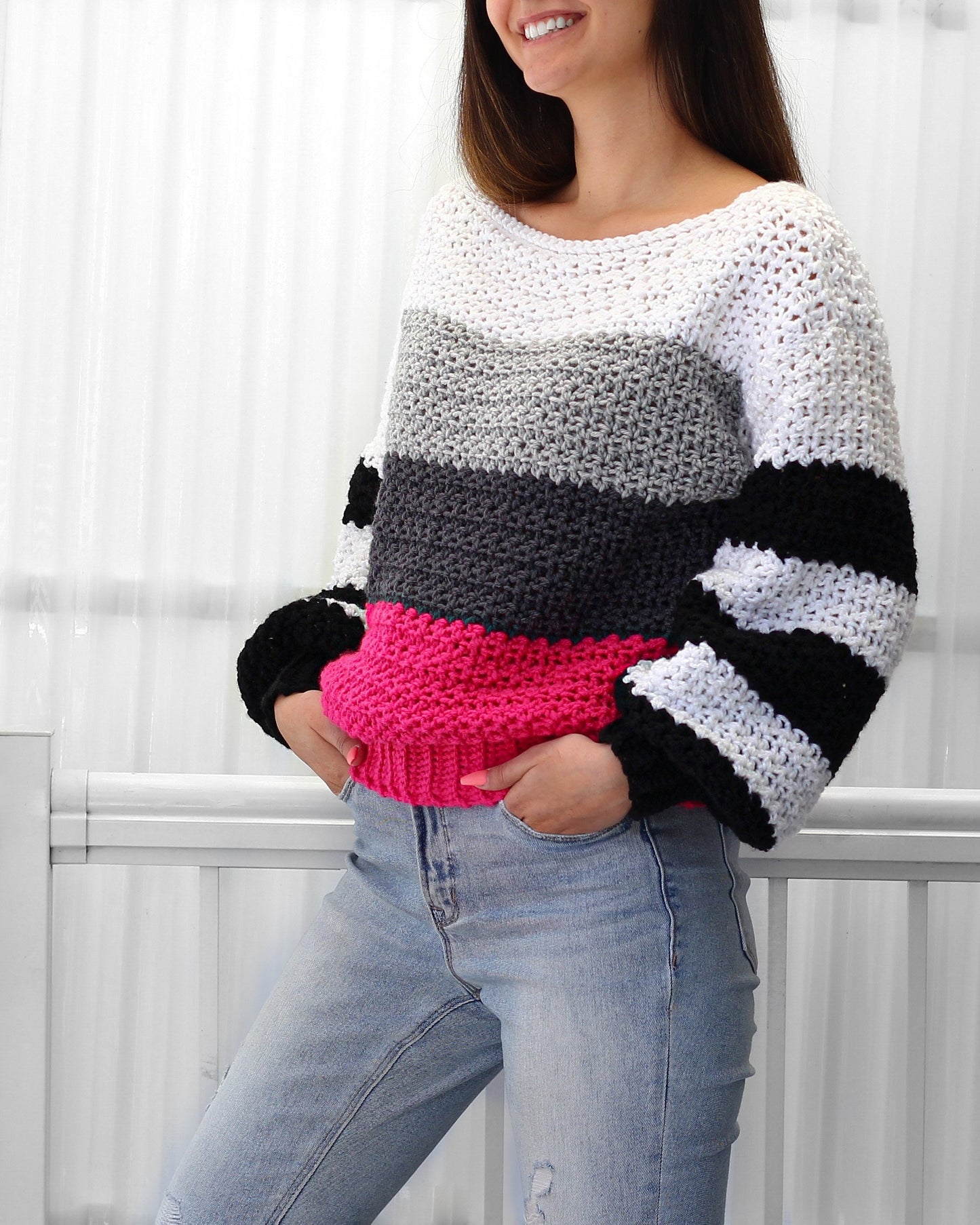 May include: A striped crochet sweater with a white, gray, black, and pink color scheme. The sweater has a boat neck and long sleeves.