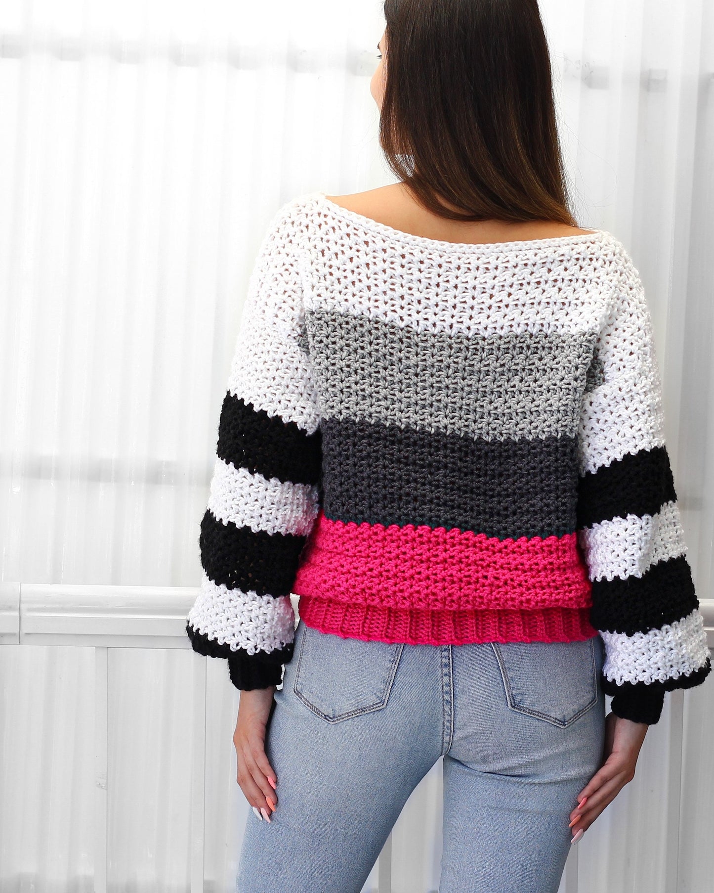 May include: A striped crochet sweater with a pink, gray, and white color scheme. The sweater has a loose fit and long sleeves.