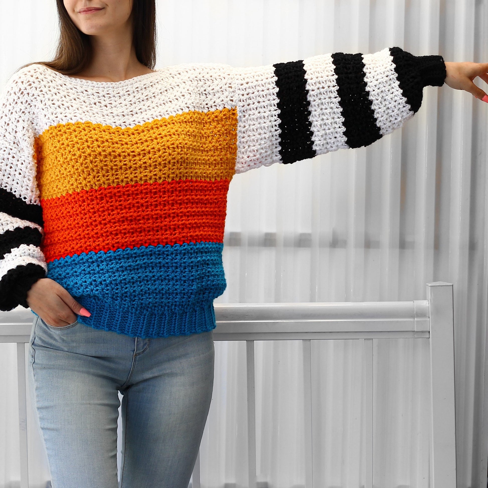 May include: A colorful striped crochet sweater with long sleeves and a relaxed fit. The sweater features a white base with horizontal stripes of yellow, orange, and blue.