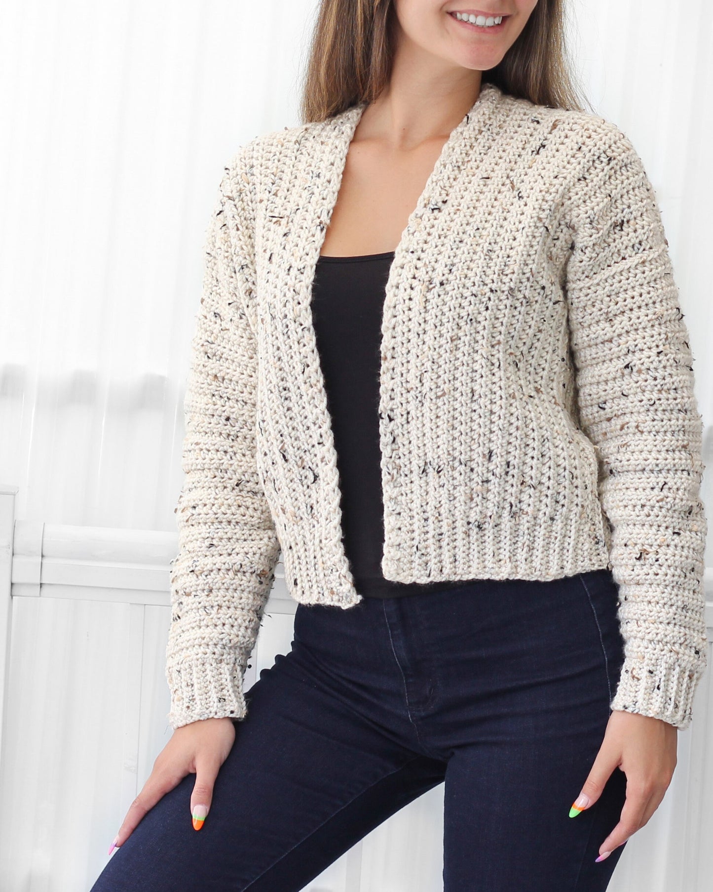 May include: A cream-colored crocheted cardigan with a speckled pattern. The cardigan has a V-neck and long sleeves.