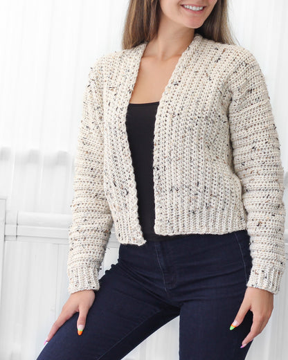 May include: A cream-colored crocheted cardigan with a speckled pattern. The cardigan has a V-neck and long sleeves.