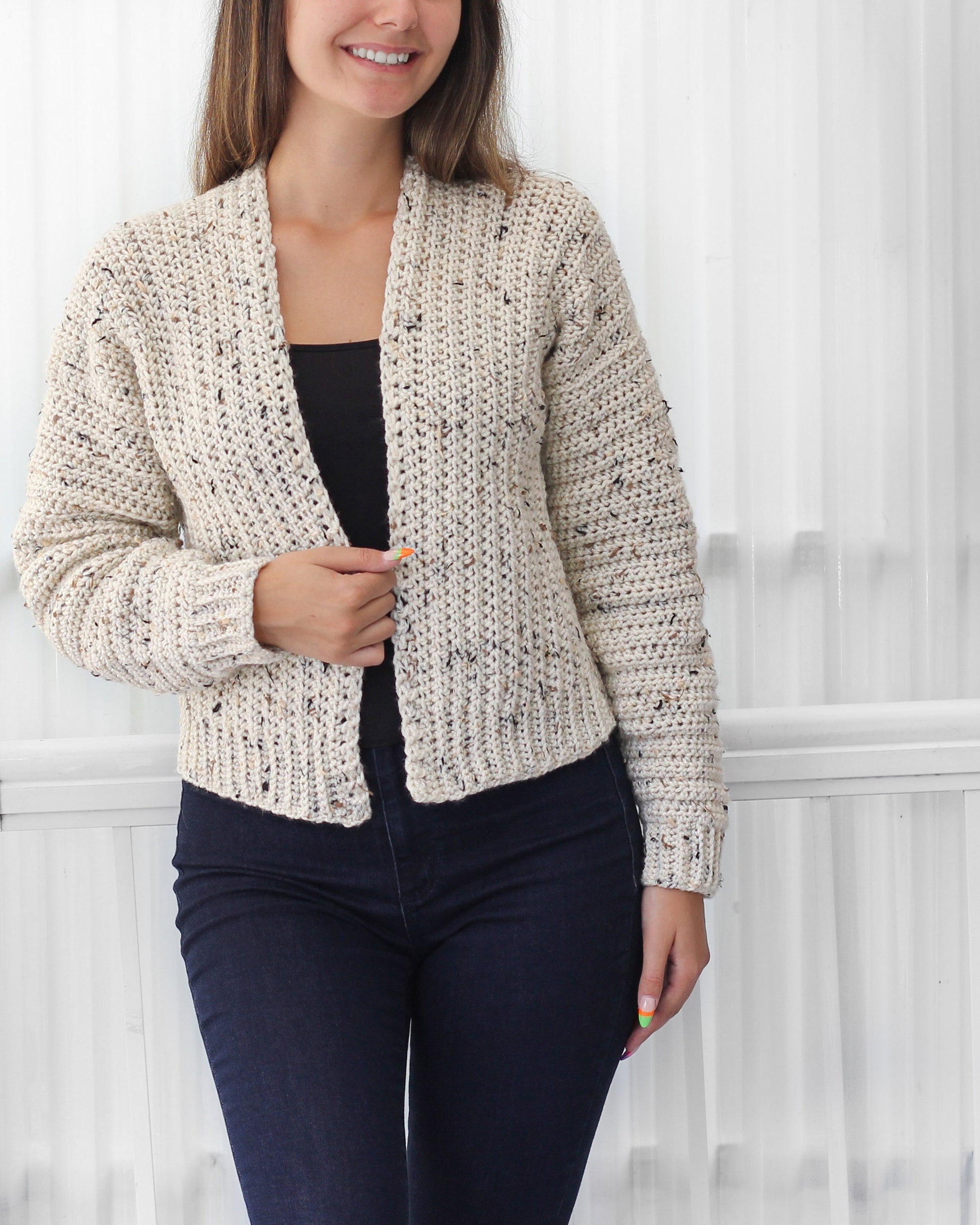 May include: A cream-colored crochet cardigan with a speckled pattern. The cardigan has a V-neck and long sleeves.