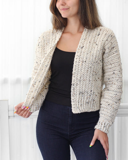 May include: A cream-colored crocheted cardigan with a speckled pattern. The cardigan has a long sleeve and an open front.