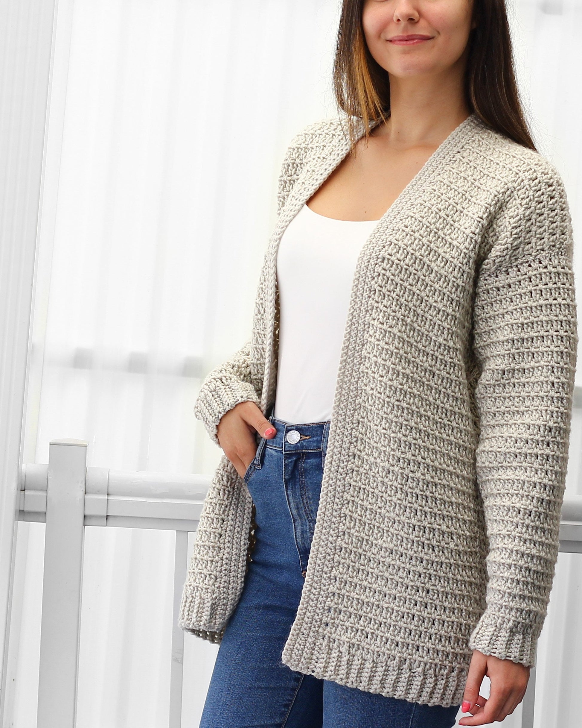 May include: A light gray crocheted cardigan with a V-neck and long sleeves. The cardigan is open in the front and has a textured stitch pattern.