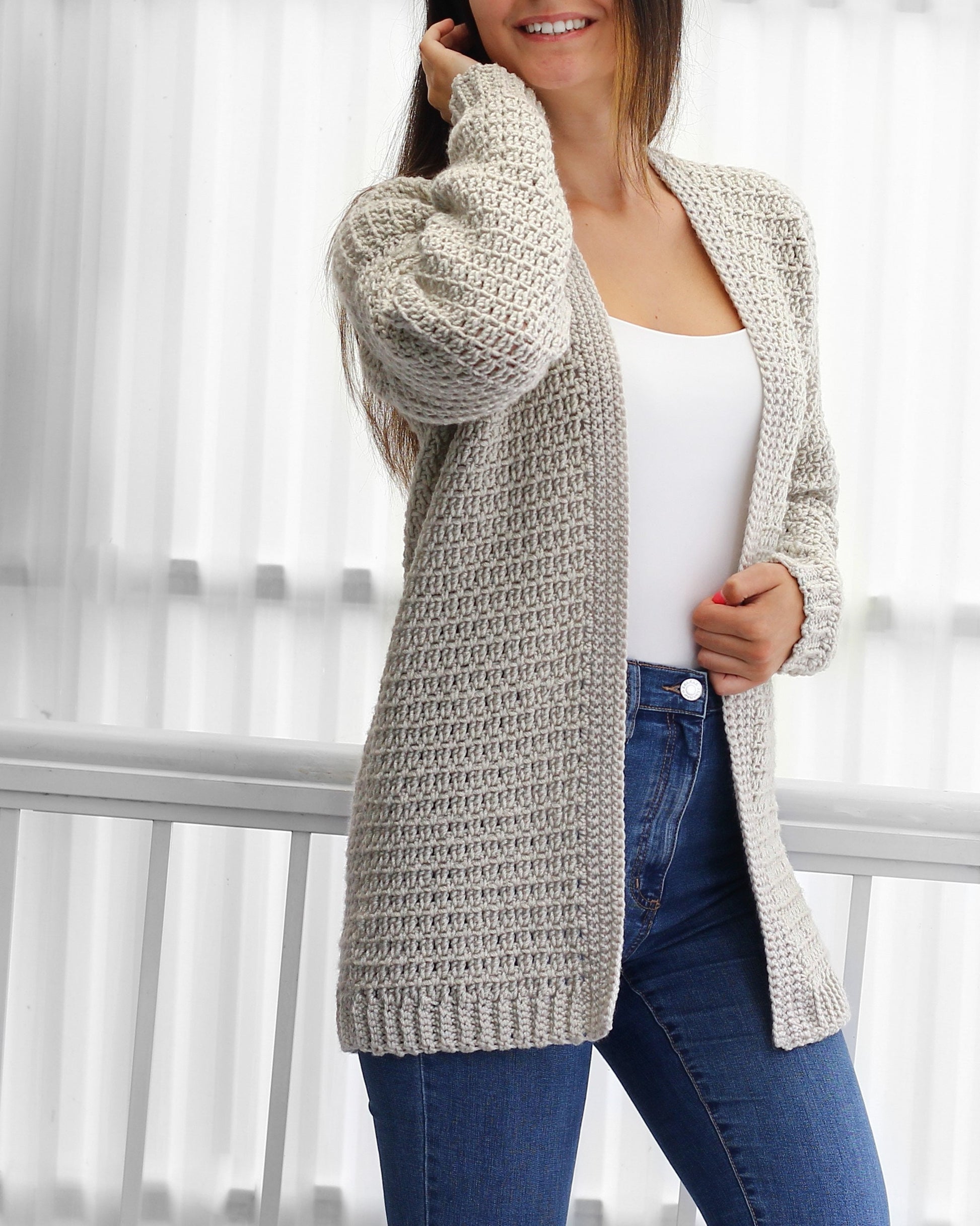 May include: A light gray crocheted cardigan with a long, open front and long sleeves. The cardigan is made with a textured stitch pattern.