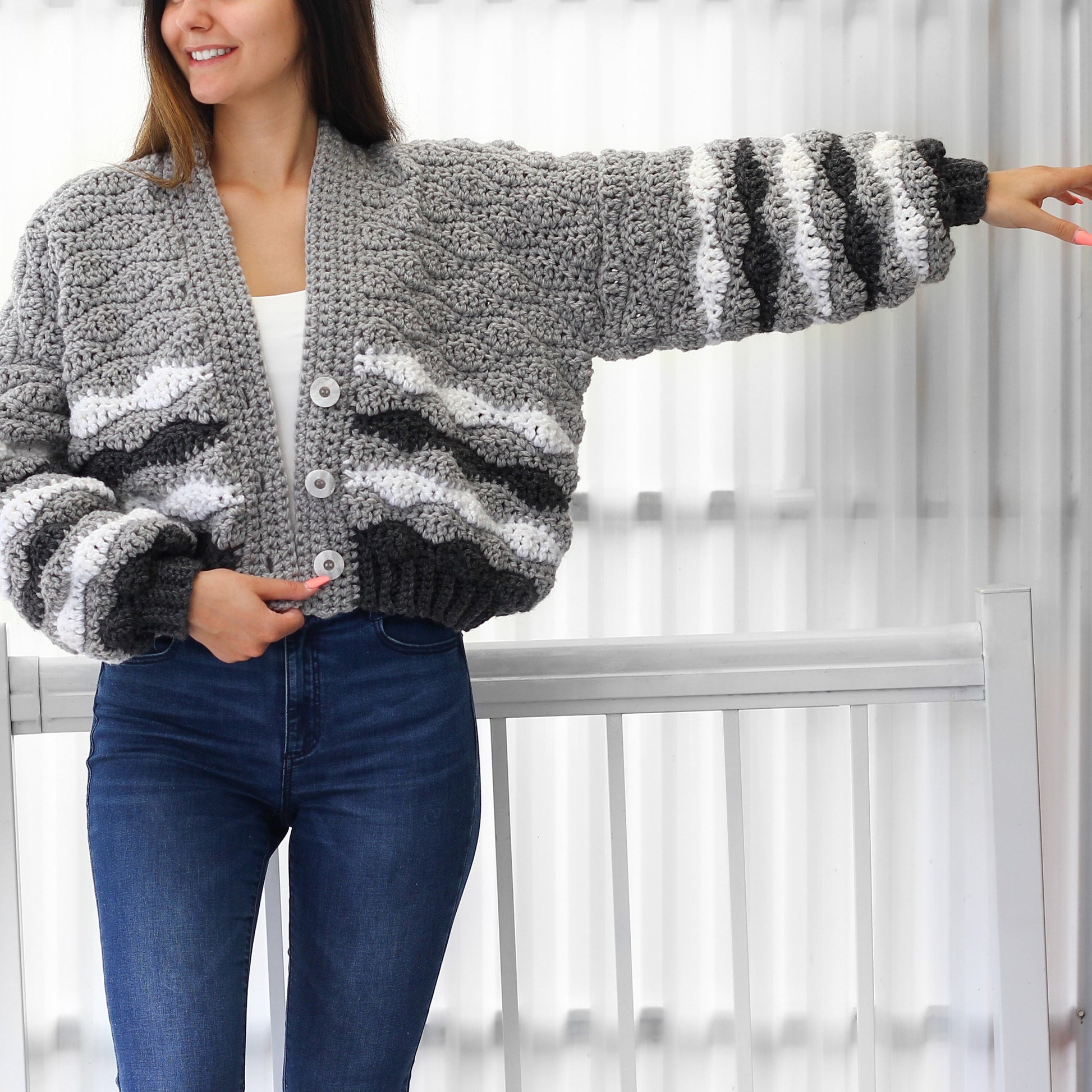 May include: A gray and white striped crocheted cardigan with a button closure. The cardigan has a relaxed fit and is cropped at the waist.