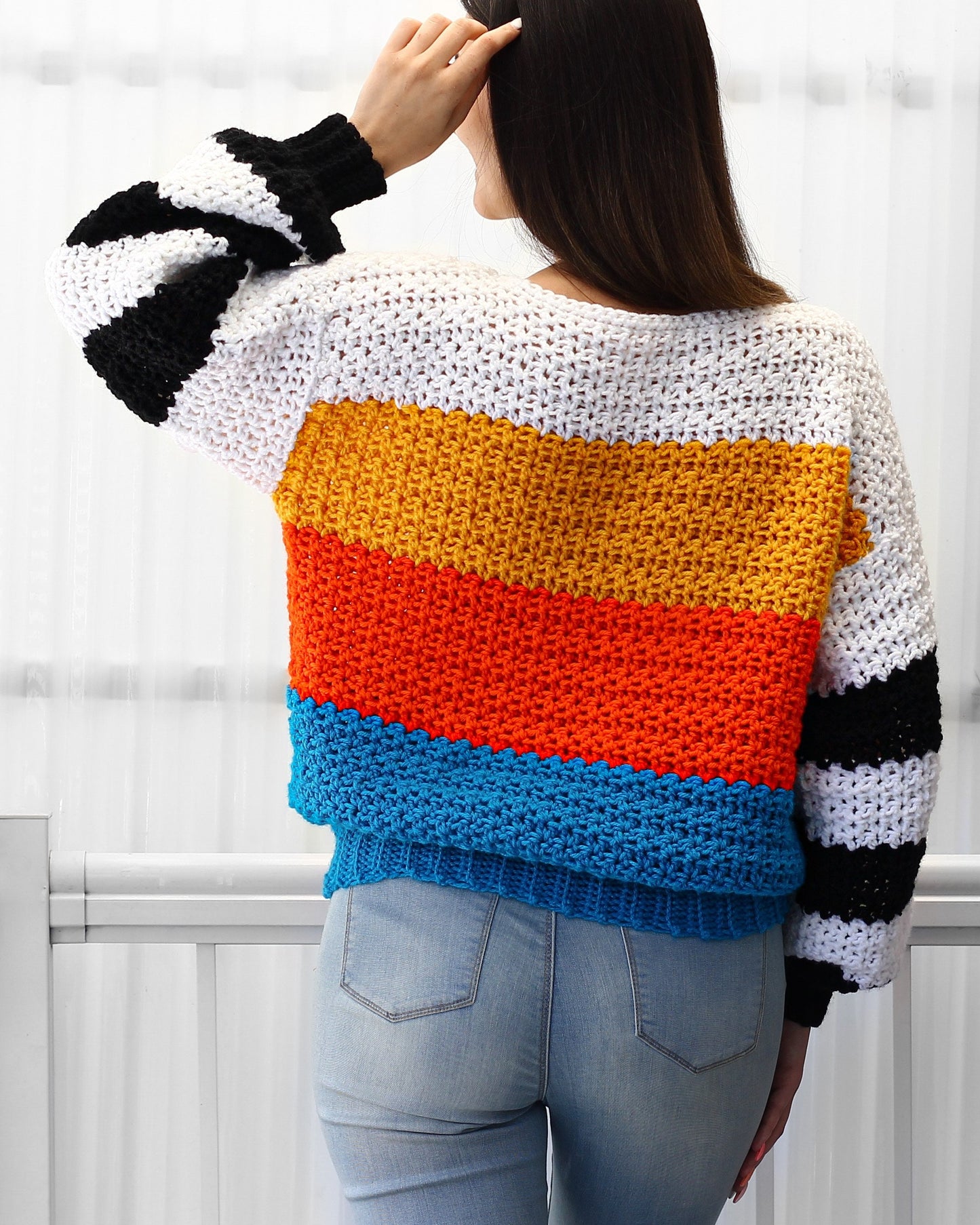 May include: A colorful striped crochet sweater with black and white stripes on the sleeves. The sweater is made with a variety of colors, including white, yellow, orange, red, and blue.