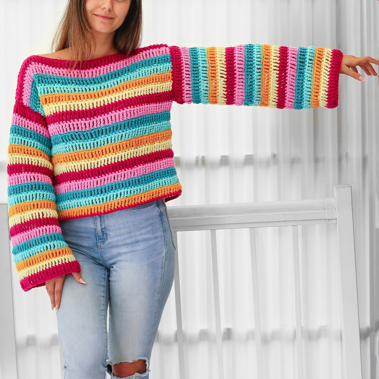 May include: A rainbow striped crochet sweater with long sleeves. The sweater is cropped and has a loose fit.