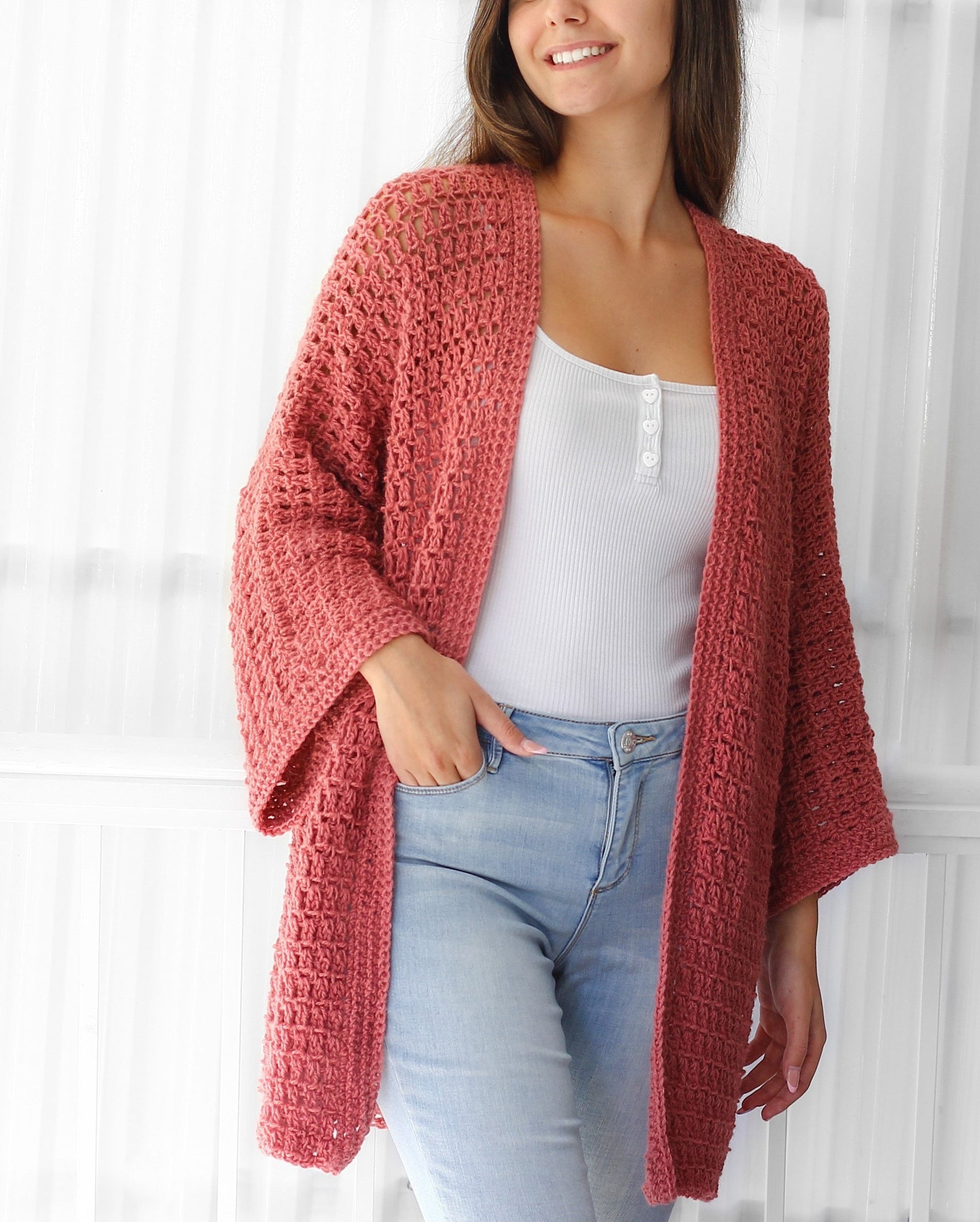 May include: A crocheted cardigan in a dusty rose color with a loose fit and long sleeves. The cardigan is open in the front and has a simple, elegant design.
