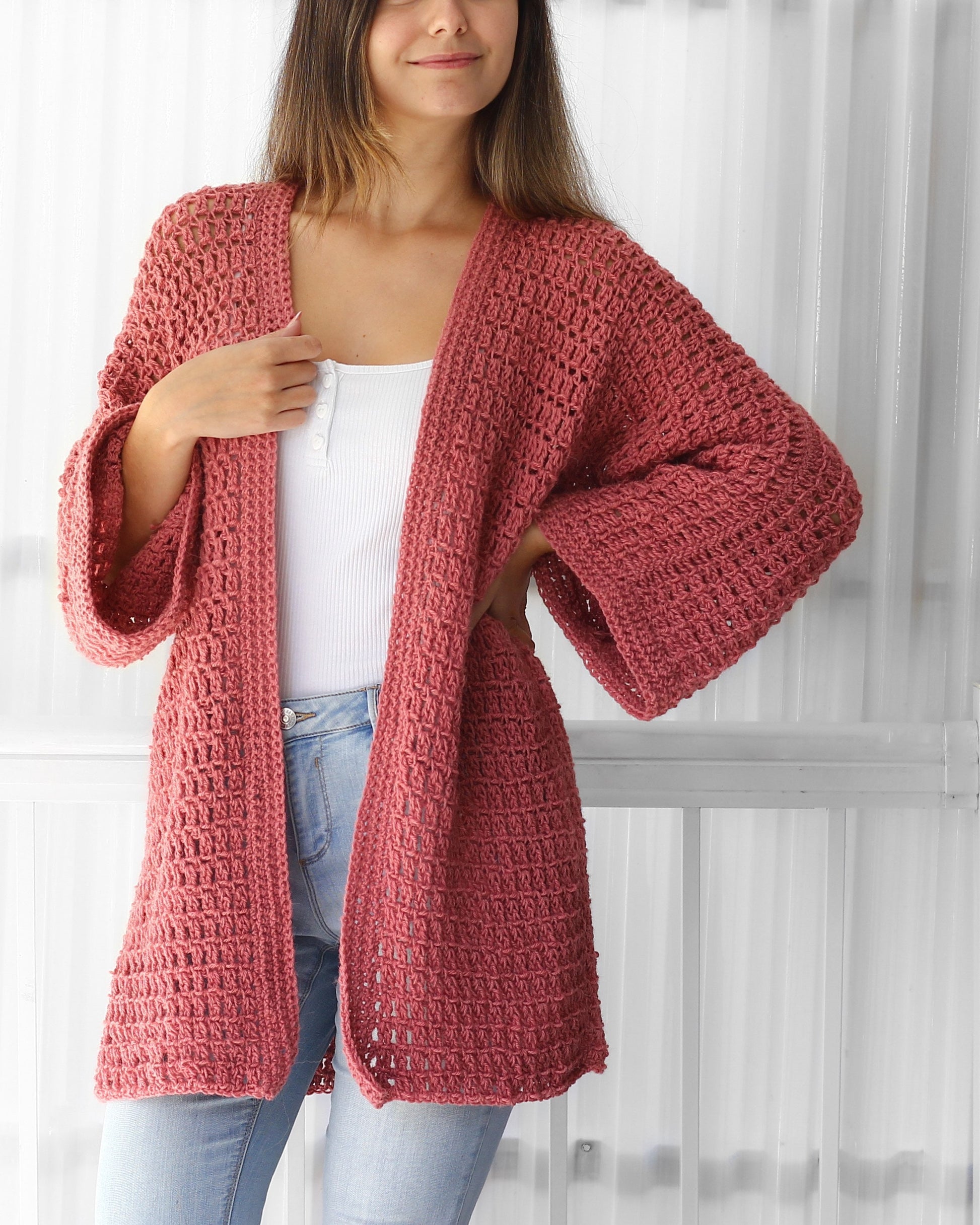 May include: A crocheted cardigan in a dusty rose color with a loose fit and long sleeves. The cardigan is open in the front and has a simple stitch pattern.