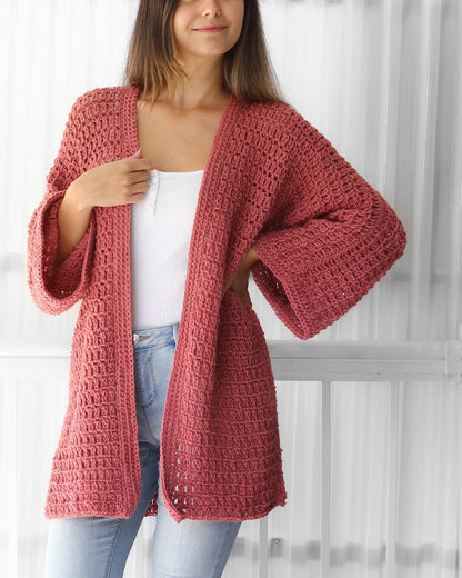 May include: A crocheted cardigan in a dusty rose color with a loose fit and long sleeves. The cardigan is open in the front and has a simple stitch pattern.