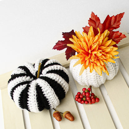 May include: Two crocheted pumpkins, one black and white striped and one white, with a crocheted flower arrangement in a white pot. The flower arrangement features a yellow chrysanthemum and red fall leaves.