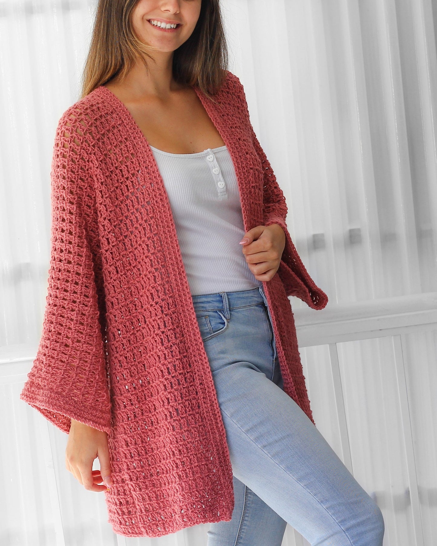 May include: A dusty rose crochet cardigan with a loose fit and wide sleeves. The cardigan is open in the front and has a simple, elegant design.