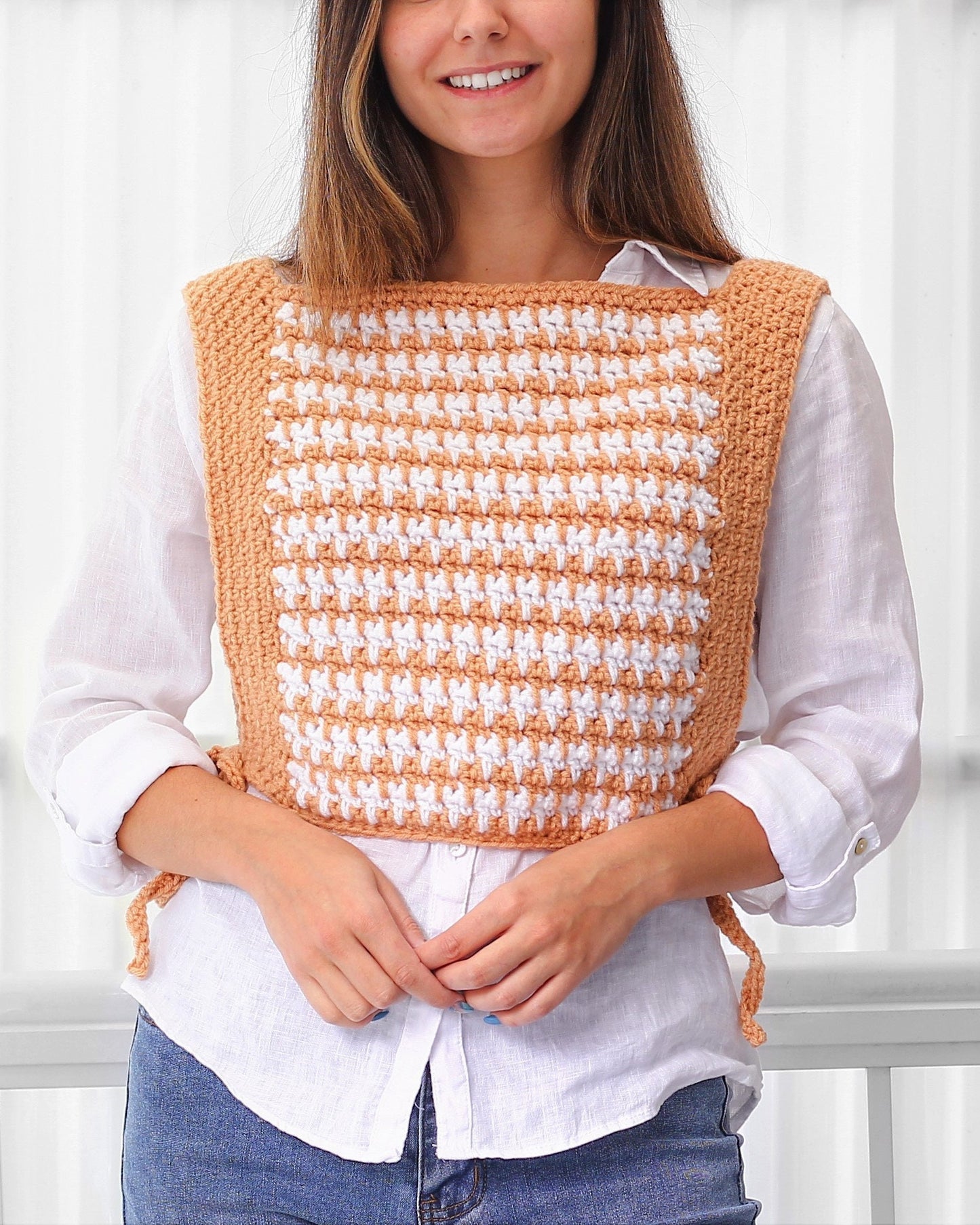 May include: A crocheted vest with a houndstooth pattern in peach and white. The vest has a square neckline and ties at the sides.