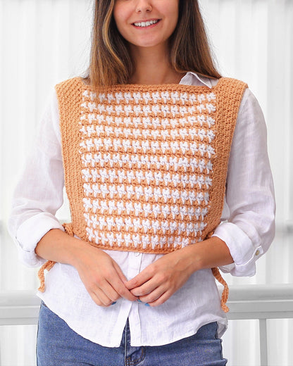 May include: A crocheted vest with a houndstooth pattern in peach and white. The vest has a square neckline and ties at the sides.