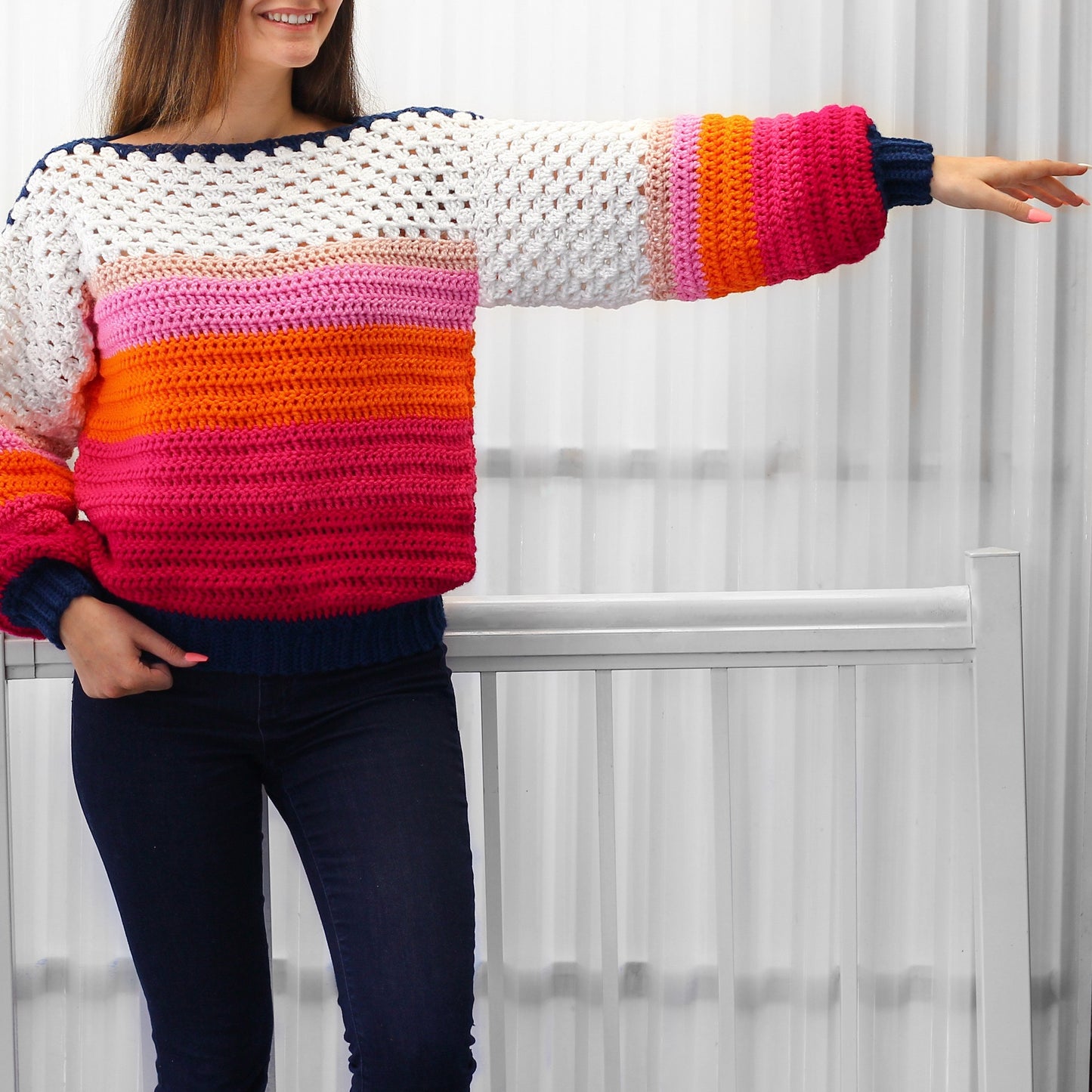 May include: A colorful striped crochet sweater with long sleeves and a wide neckline. The sweater is made with a variety of colors, including white, pink, orange, and blue.