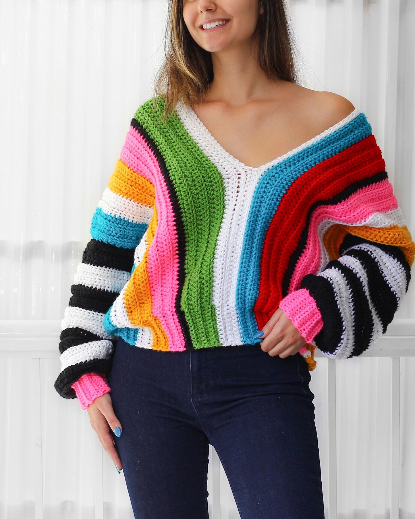 May include: A colorful striped crochet sweater with a V-neck and long sleeves. The sweater is made with a variety of bright colors, including red, orange, yellow, green, blue, and pink.
