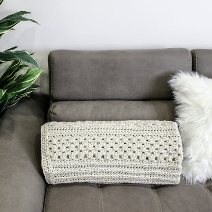 May include: A light gray crocheted throw blanket is draped over a gray couch with a white faux fur pillow.