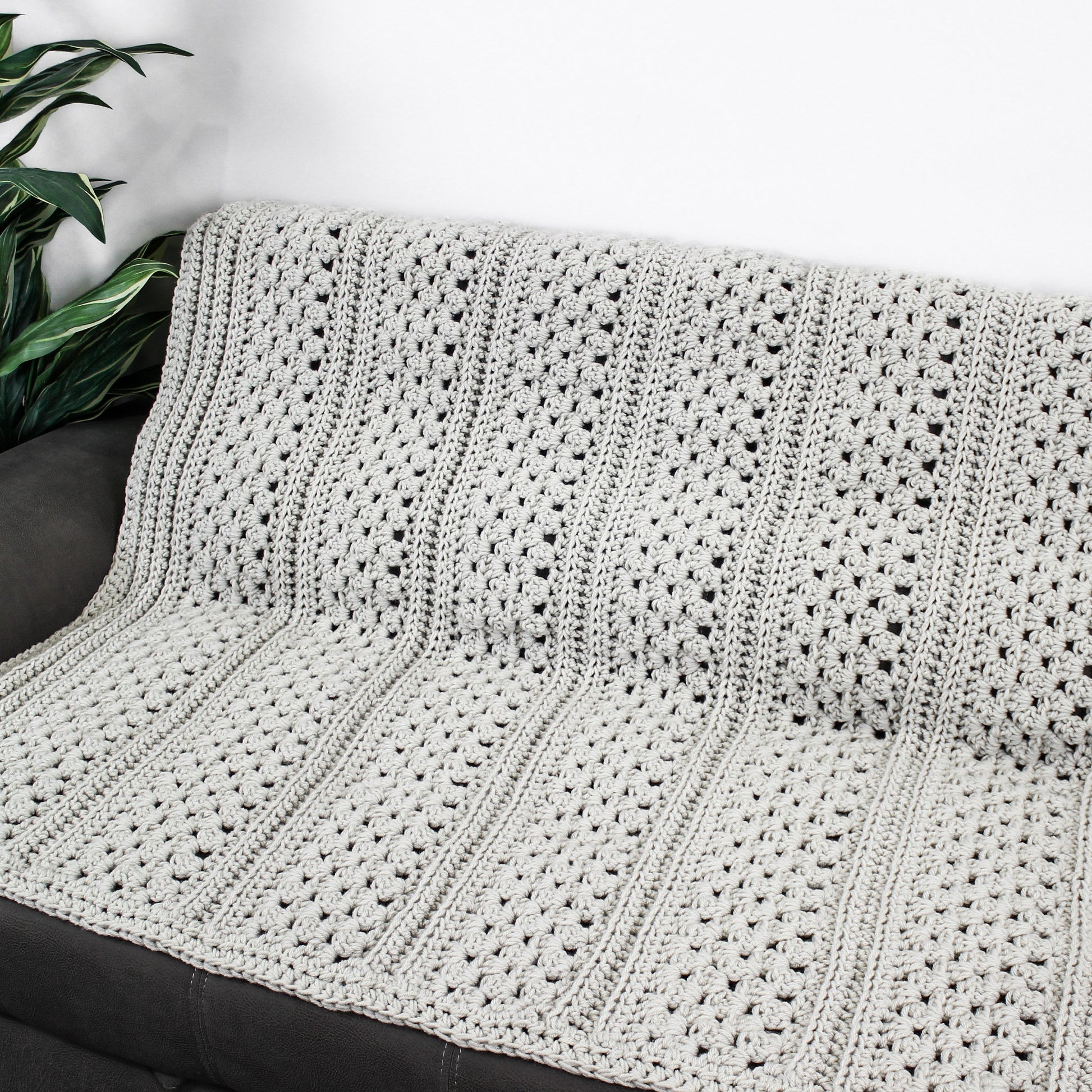 May include: A gray crocheted throw blanket with a textured pattern. The blanket is draped over a gray couch.