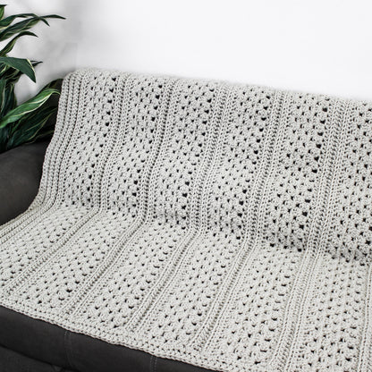 May include: A gray crocheted throw blanket with a textured pattern. The blanket is draped over a gray couch.