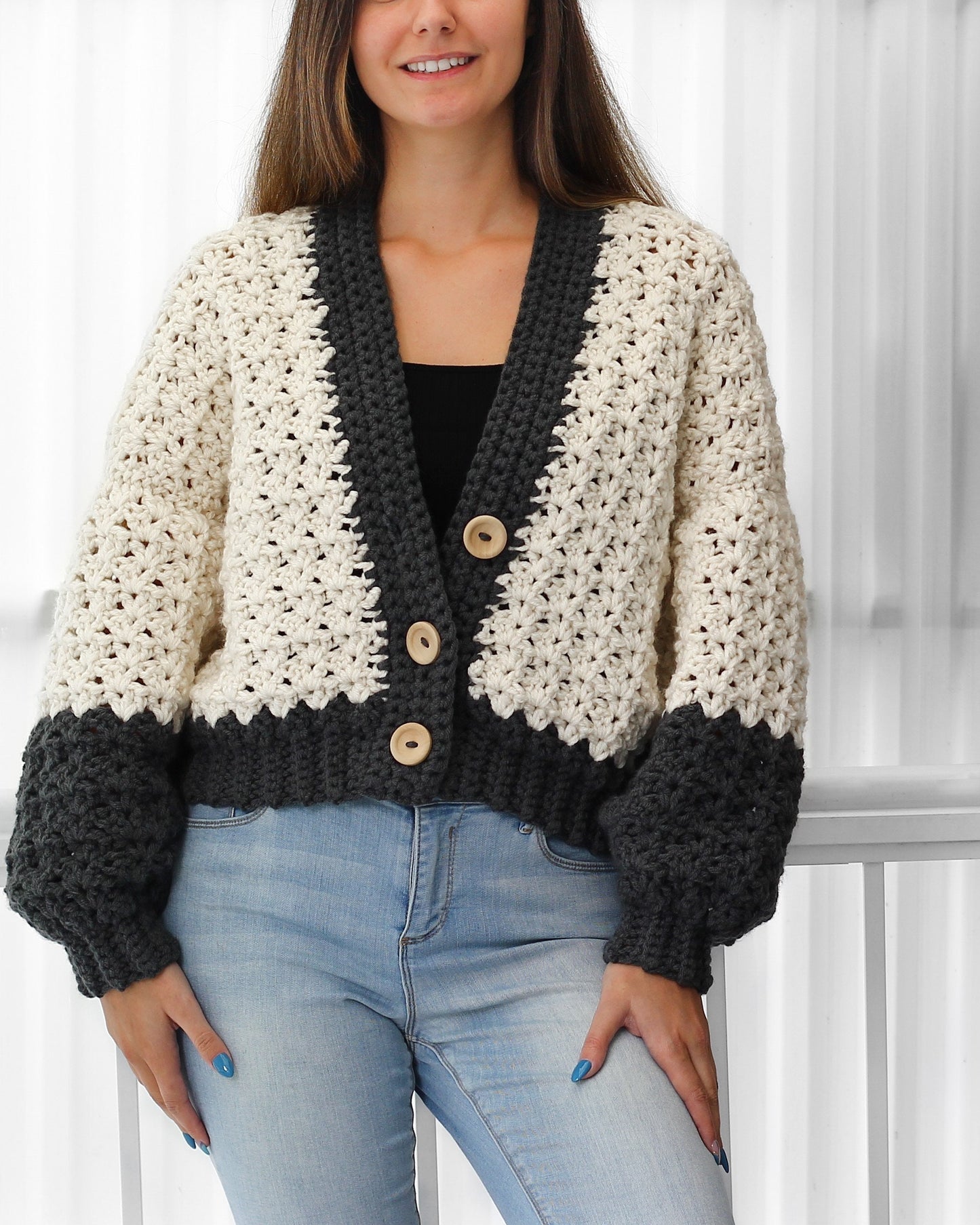 May include: A white and gray crocheted cardigan with a V-neck and button closure. The cardigan has a color block design with the sleeves and bottom band in gray.
