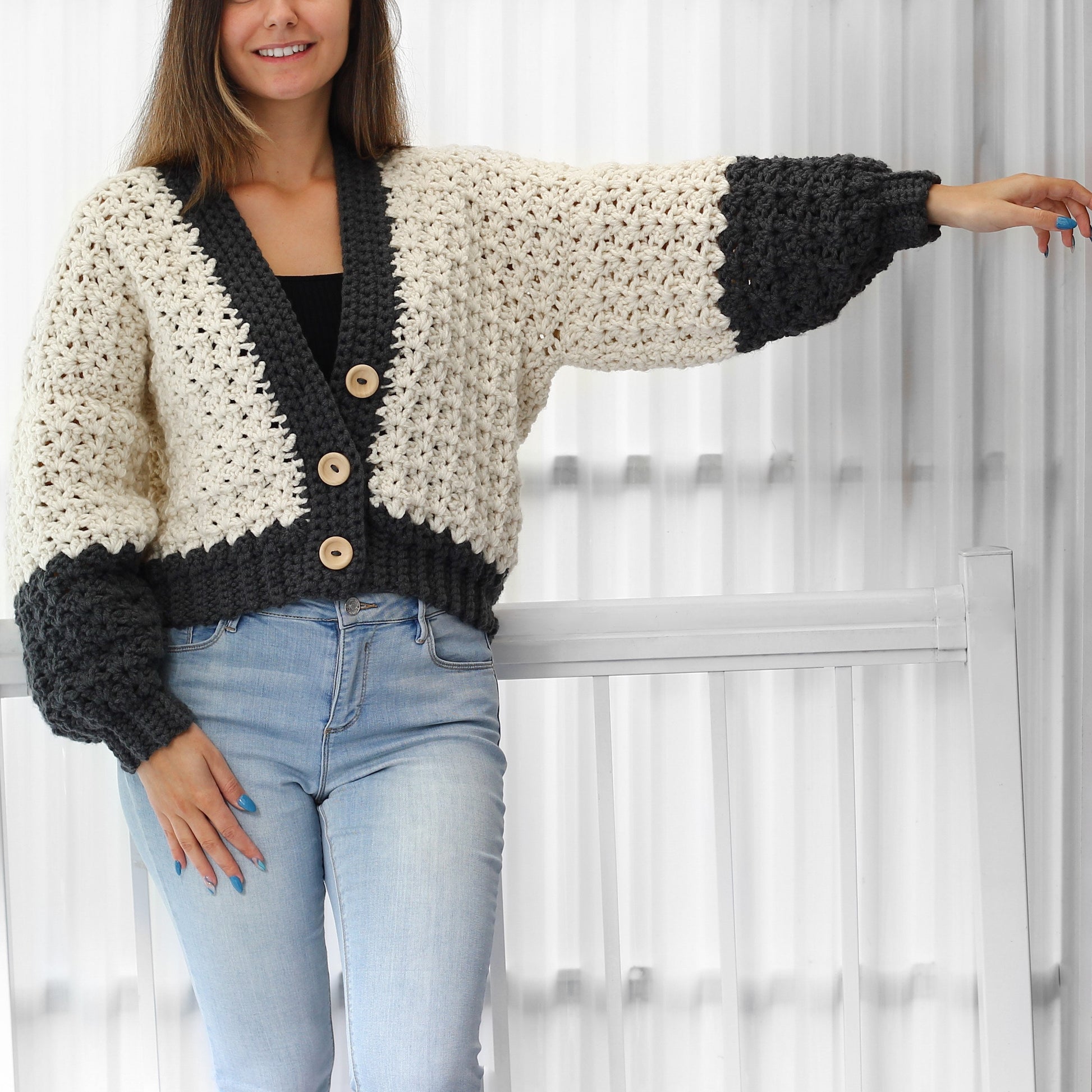 May include: A white and gray crocheted cardigan with a v-neck and button closure. The cardigan has long sleeves with a gray cuff and a cropped length.