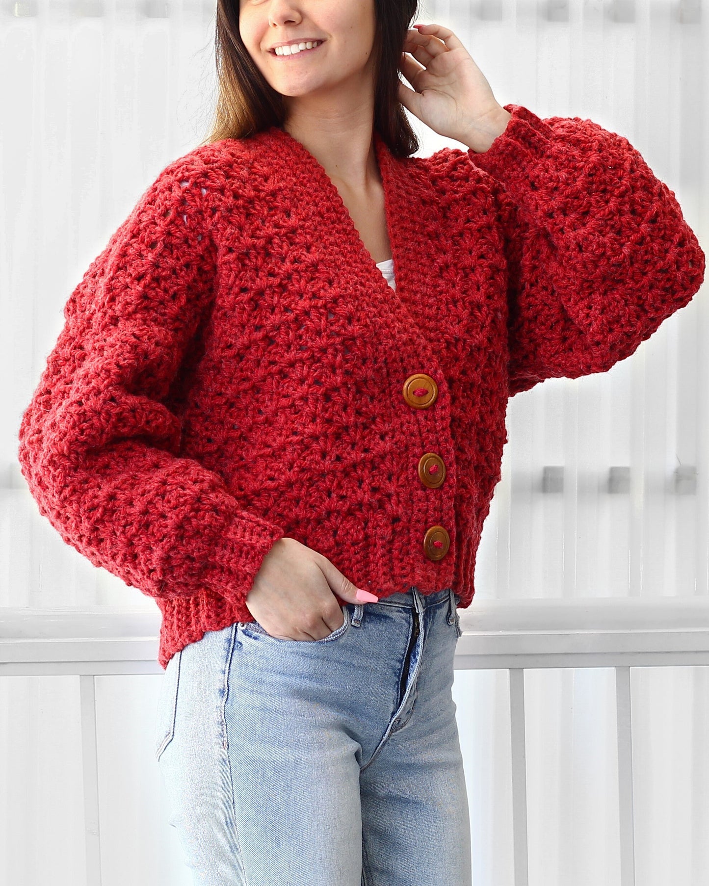 May include: A red crocheted cardigan with a V-neck and button closure. The cardigan has a textured stitch pattern and is cropped.