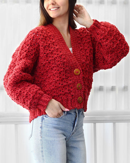 May include: A red crocheted cardigan with a V-neck and button closure. The cardigan has a textured stitch pattern and is cropped.