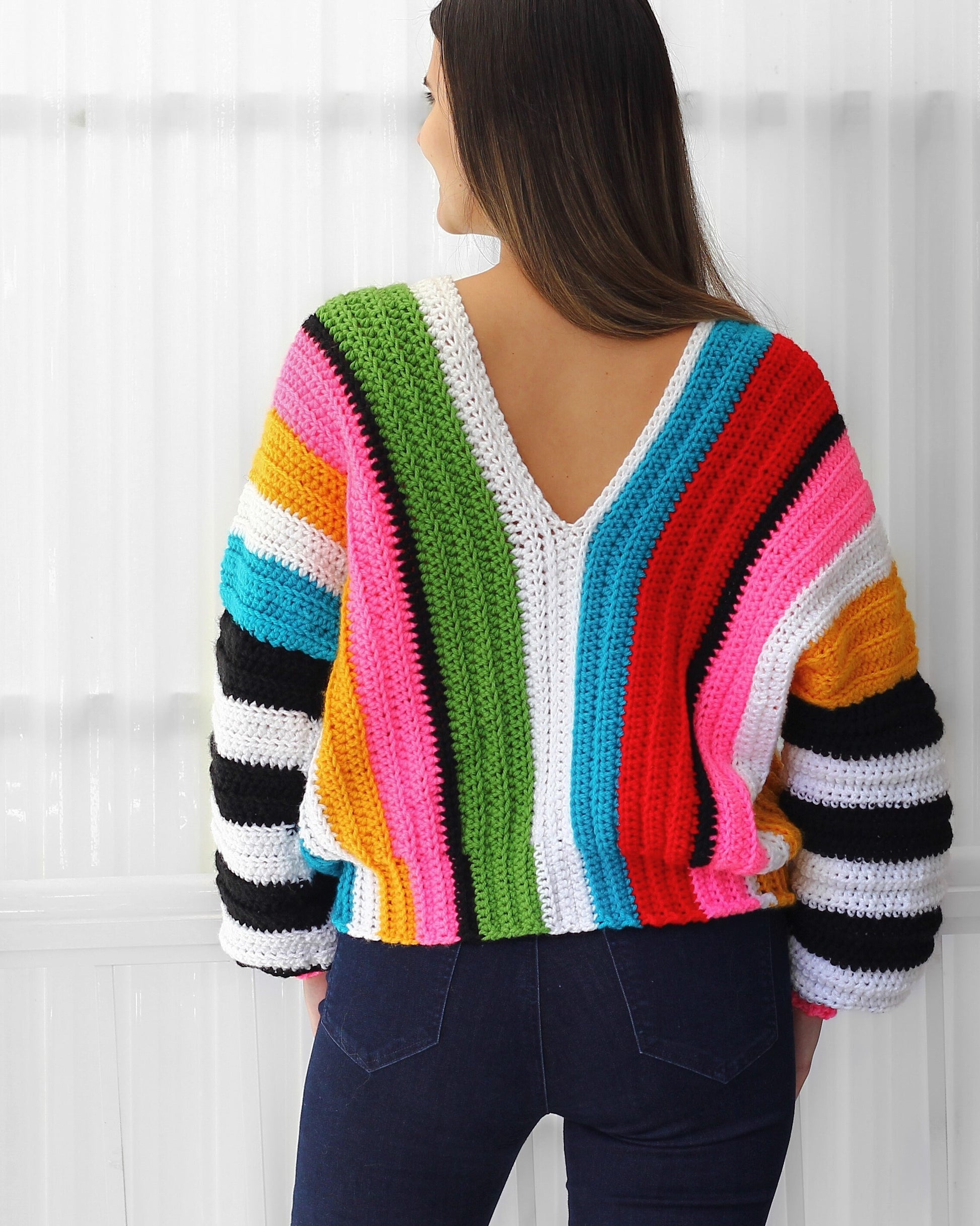 May include: A colorful striped crochet sweater with a V-neck and long sleeves. The sweater is made with a variety of bright colors, including red, yellow, blue, green, and pink.
