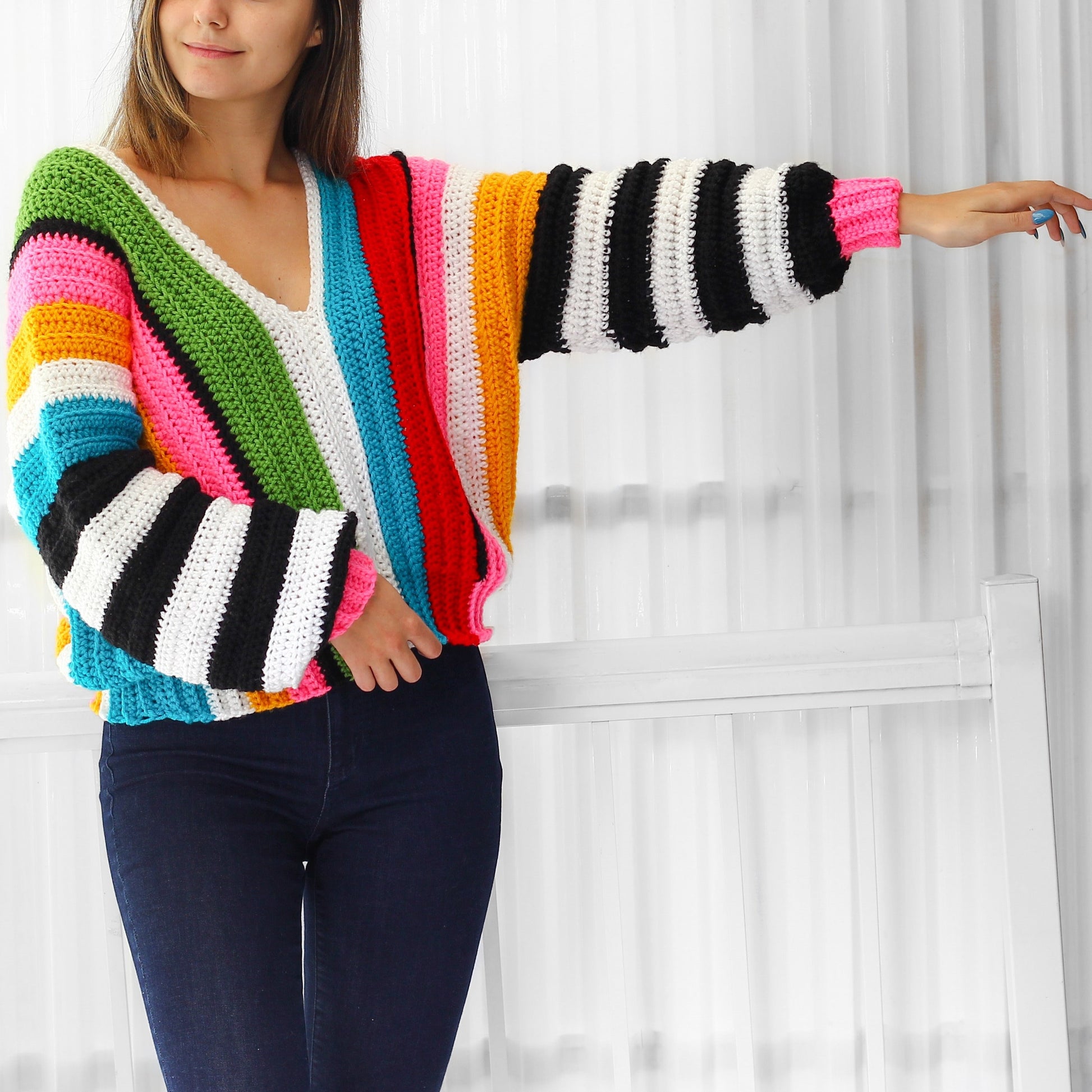May include: A colorful striped crochet sweater with a V-neck and long sleeves. The sweater is made with a variety of colors, including red, orange, yellow, green, blue, and pink.