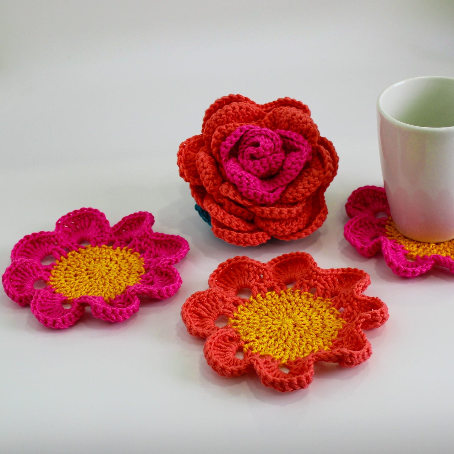 May include: Four crocheted flower coasters in shades of pink, orange, and yellow. The coasters are made with a delicate, lacy stitch and feature a central circle.