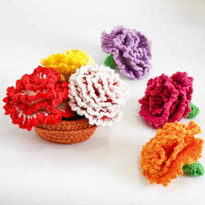 May include: Five crocheted carnation flowers in various colors, including red, white, yellow, orange, and purple. The flowers are arranged in a small brown crocheted basket.