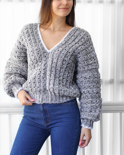 May include: A gray and white crocheted sweater with a V-neck and long sleeves. The sweater has a white trim around the neckline and cuffs.