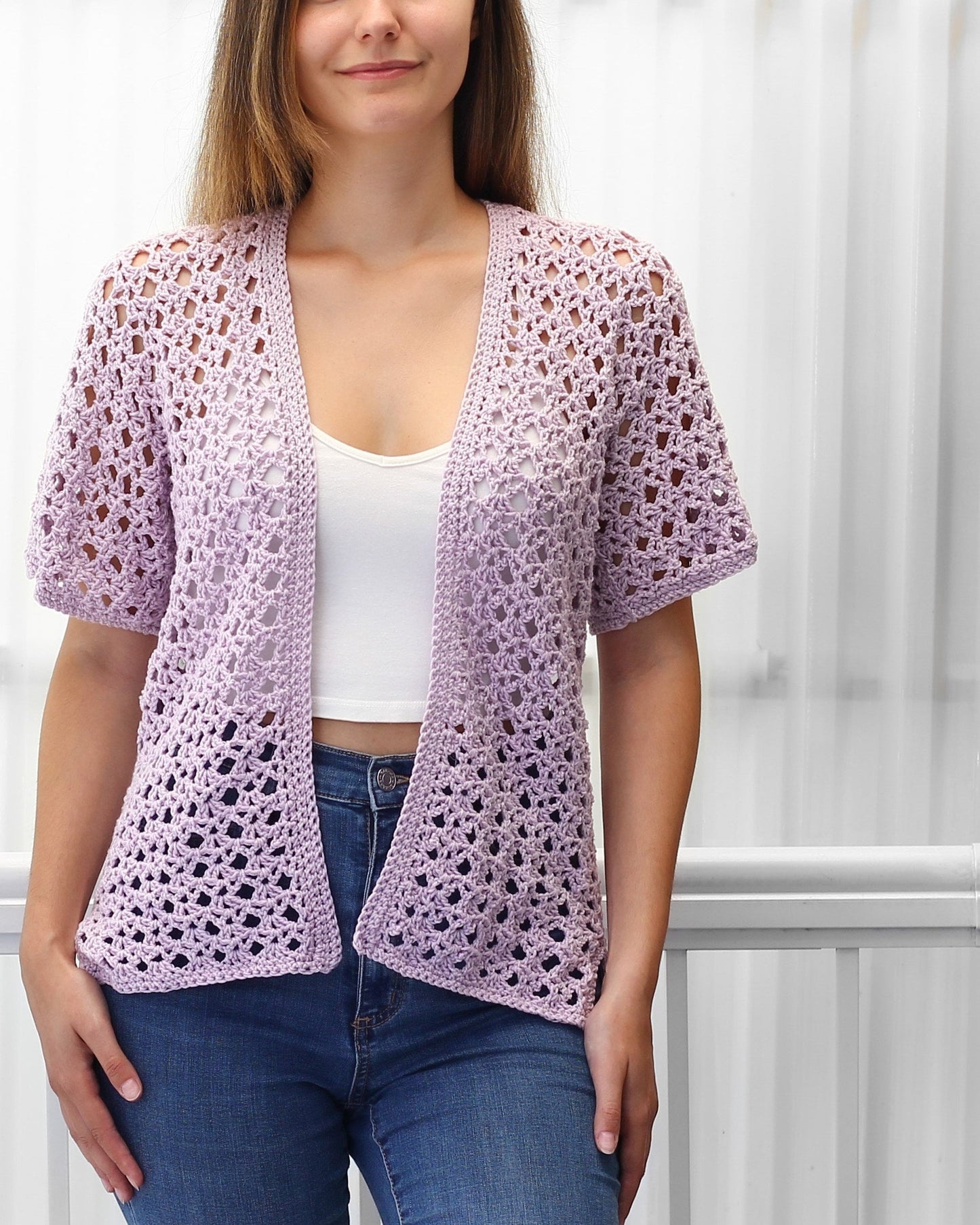 May include: A light purple crochet cardigan with a V-neck and short sleeves. The cardigan is made with a delicate open stitch pattern.