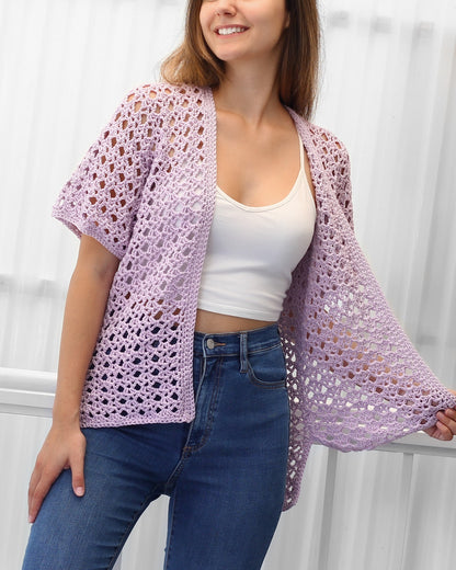May include: A light purple crochet cardigan with a lacy open stitch pattern. The cardigan has short sleeves and a relaxed fit.