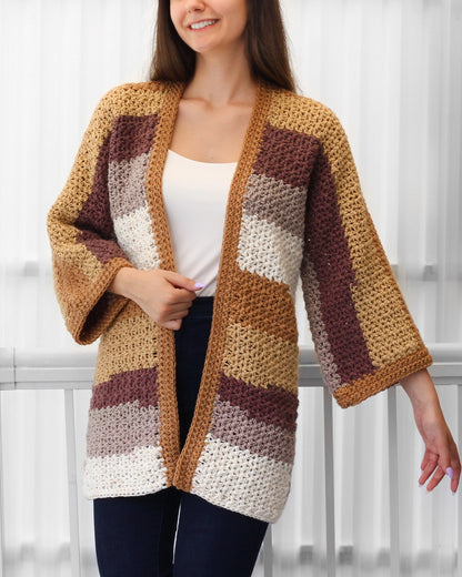 May include: A handmade, open-front crochet cardigan in a patchwork design. The color palette includes shades of tan, brown, cream, and mauve. The cardigan features three-quarter length sleeves and a relaxed fit, perfect for layering.