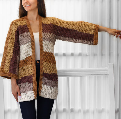 May include: A handmade, open-front crochet cardigan in a mix of warm, earthy tones. The color blocks include shades of tan, brown, and cream. The cardigan features wide sleeves and a relaxed fit, perfect for layering.