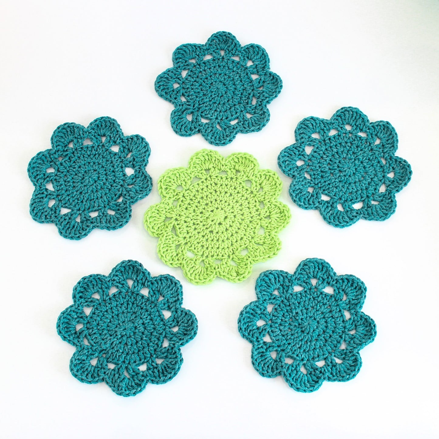 May include: Six crocheted coasters in teal and green. The coasters are round and have a scalloped edge. They are perfect for adding a touch of handmade charm to your home decor.