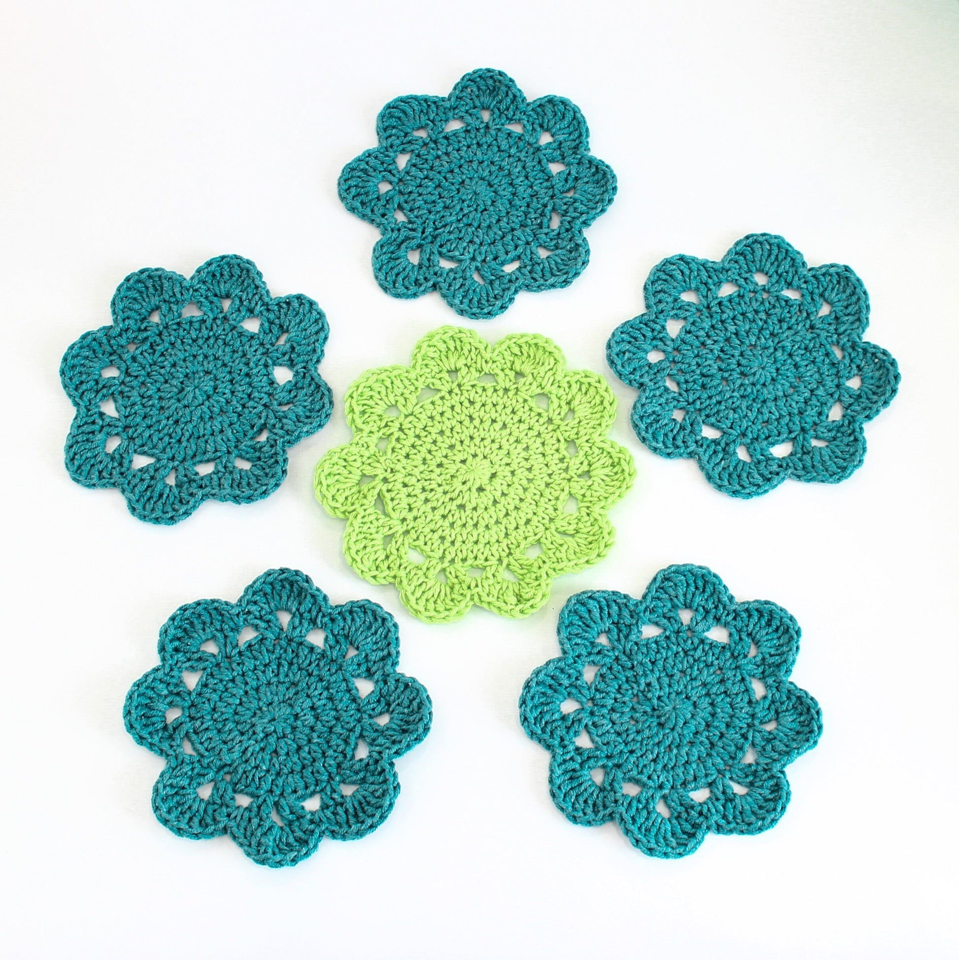 May include: Six crocheted coasters in teal and green. The coasters are round and have a scalloped edge. They are perfect for adding a touch of handmade charm to your home decor.