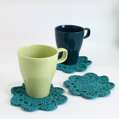 May include: Two ceramic mugs, one green and one light green, sitting on teal crocheted coasters.
