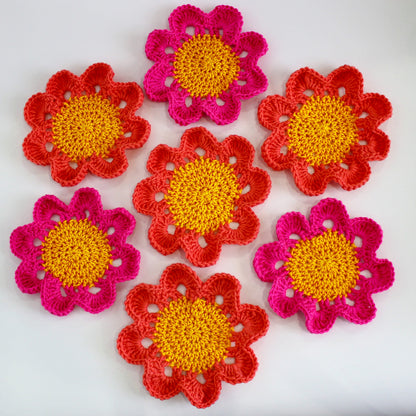 May include: Six crocheted flower coasters in shades of pink and yellow. The coasters are made with a textured yarn and have a raised center.