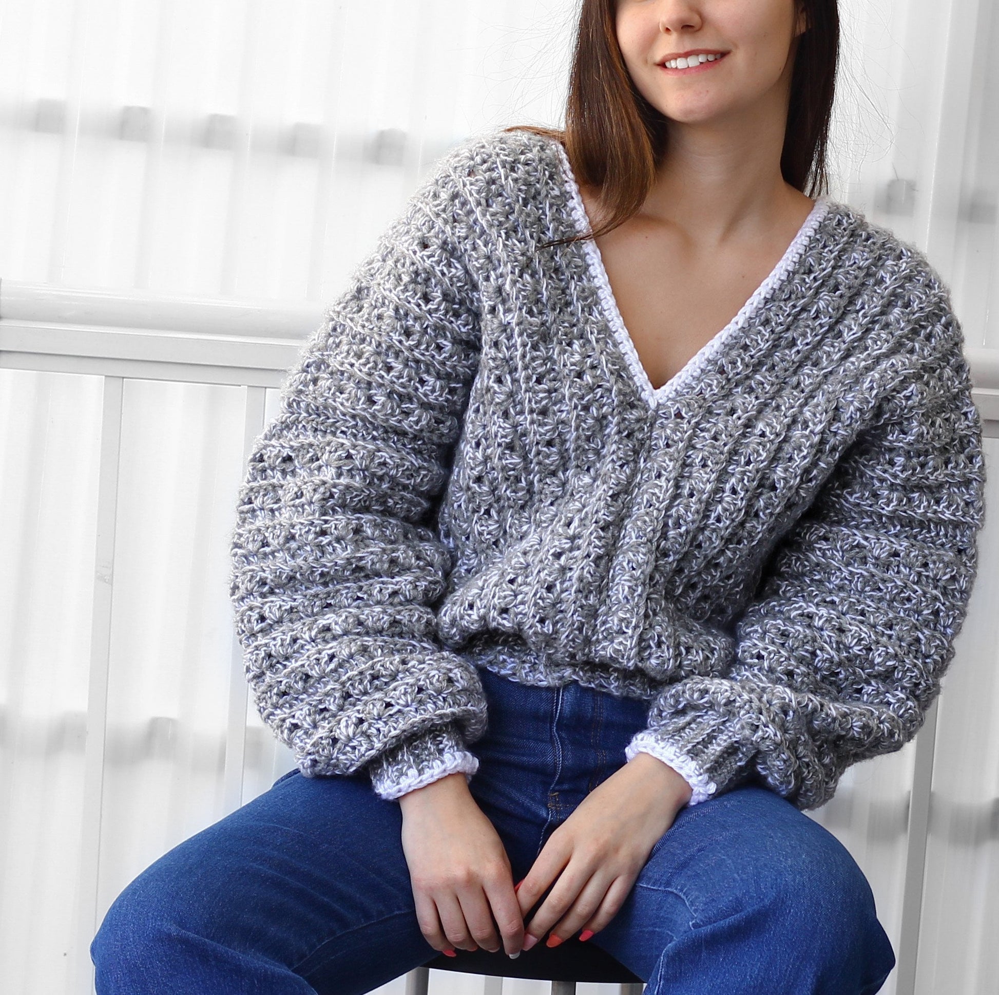 May include: A gray and white crocheted sweater with a V-neck and long sleeves. The sweater has a white crocheted trim around the neckline and cuffs.