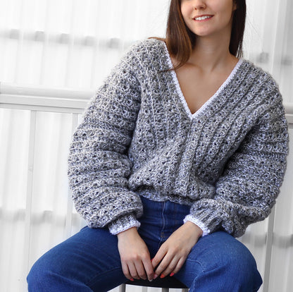May include: A gray and white crocheted sweater with a V-neck and long sleeves. The sweater has a white crocheted trim around the neckline and cuffs.