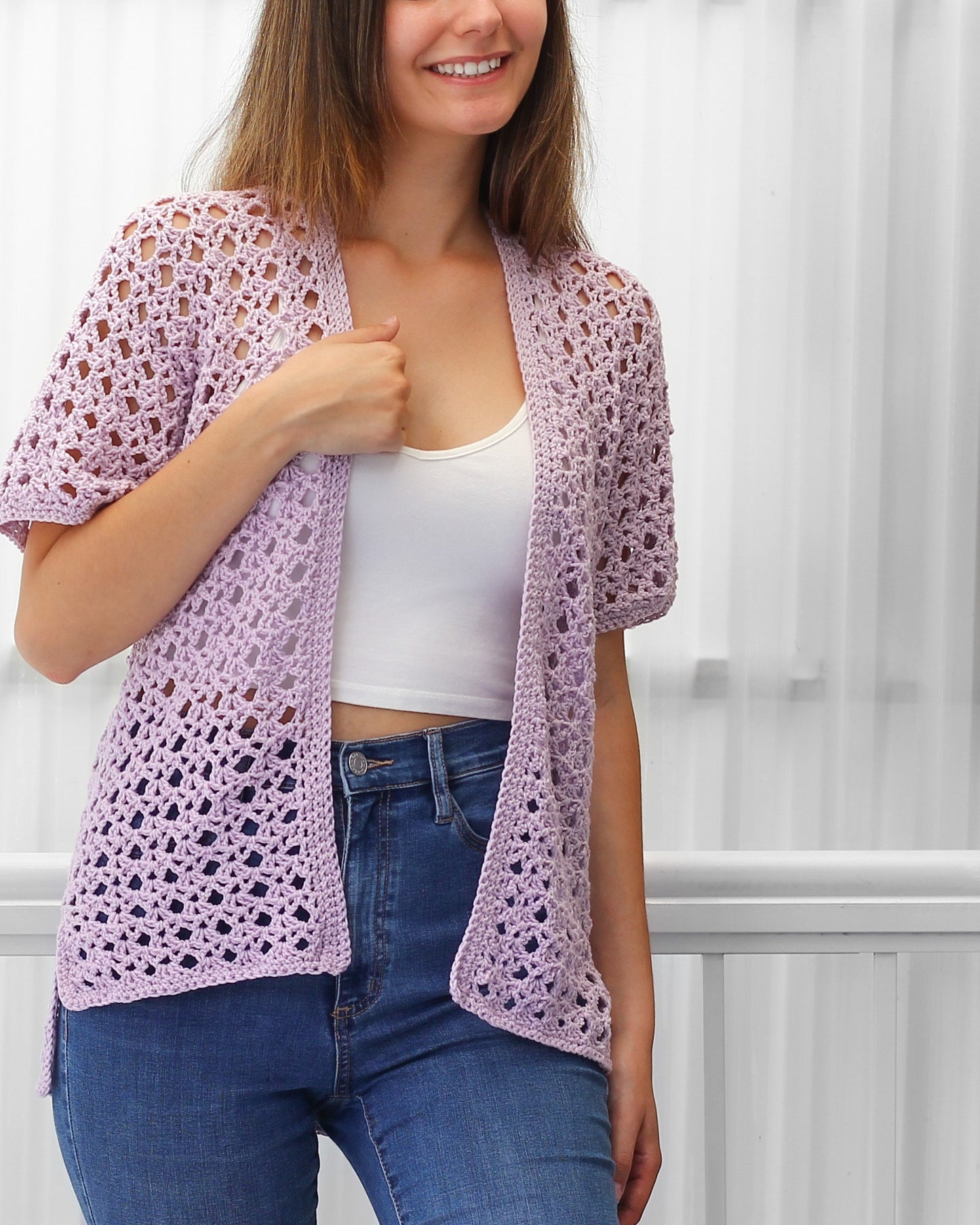 May include: A light purple crochet cardigan with a delicate openwork pattern. The cardigan has a relaxed fit and short sleeves.