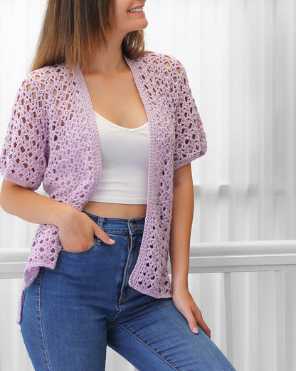 May include: A light purple crochet cardigan with a delicate openwork pattern. The cardigan has short sleeves and a relaxed fit.