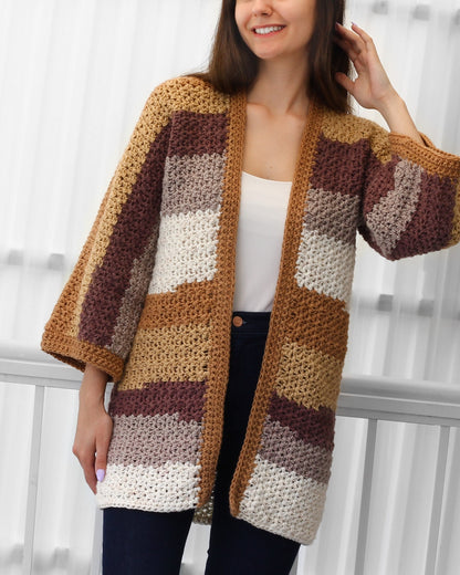 May include: A handmade, open-front crochet cardigan in a patchwork design. The color palette includes shades of tan, brown, cream, and mauve. The cardigan features wide sleeves and a textured stitch pattern, perfect for layering.
