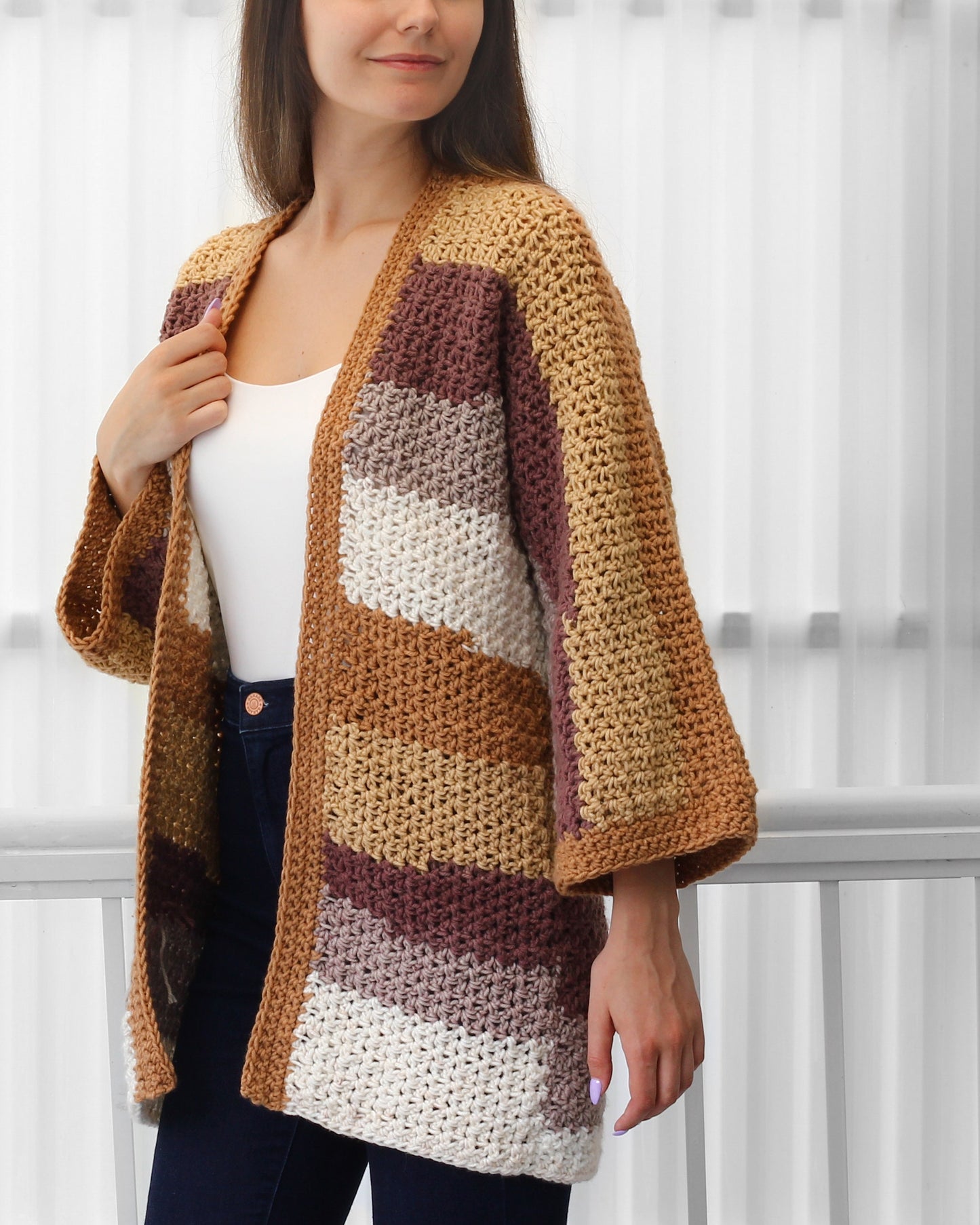 May include: A handmade, open-front crochet cardigan in a patchwork design. The color palette includes shades of tan, brown, cream, and mauve. The cardigan features wide sleeves and a textured stitch pattern, perfect for layering.