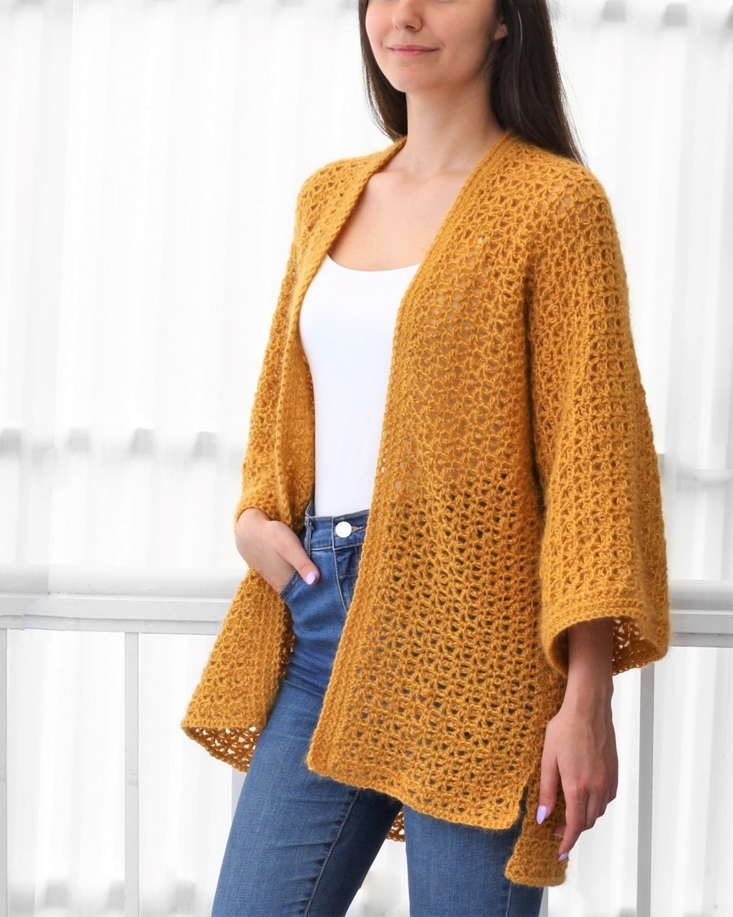 May include: A mustard yellow crochet cardigan with a loose fit and long sleeves. The cardigan has a delicate open stitch pattern and a V-neck.